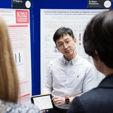 Dr Haotian Gu discusses his research poster, showing two delegates data on a tablet